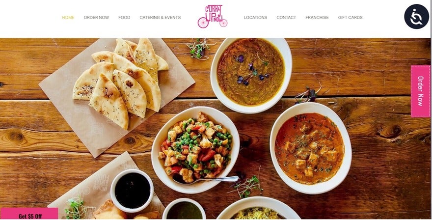 A wooden table topped with bowls of Indian food, including curry, rice, and naan bread.