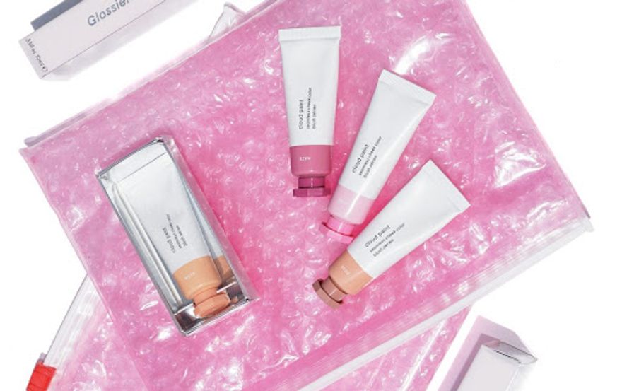 Glossier packaging pink pouch with products resting on top
